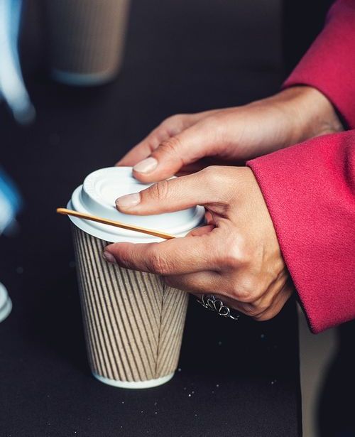Hot drink in a craft paper cup with a white cap in the hands of a young girl in a red coat.